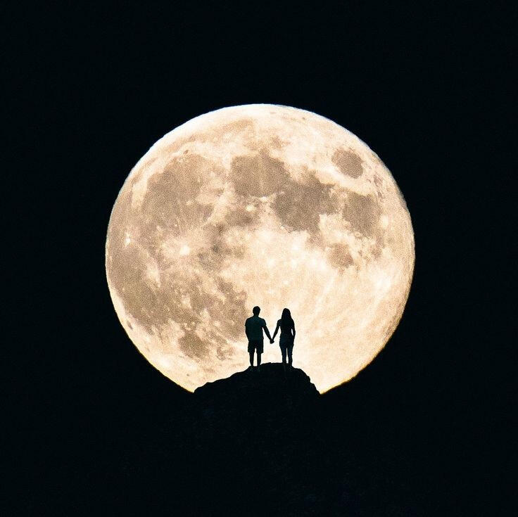 a full moon with two people's silhouettes holding hands on a black background